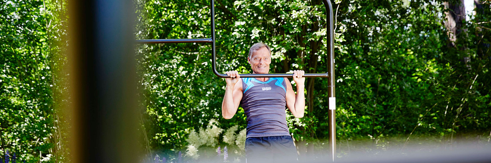 A man completes pull ups at an outdoor exercise frame with bars at various heights.